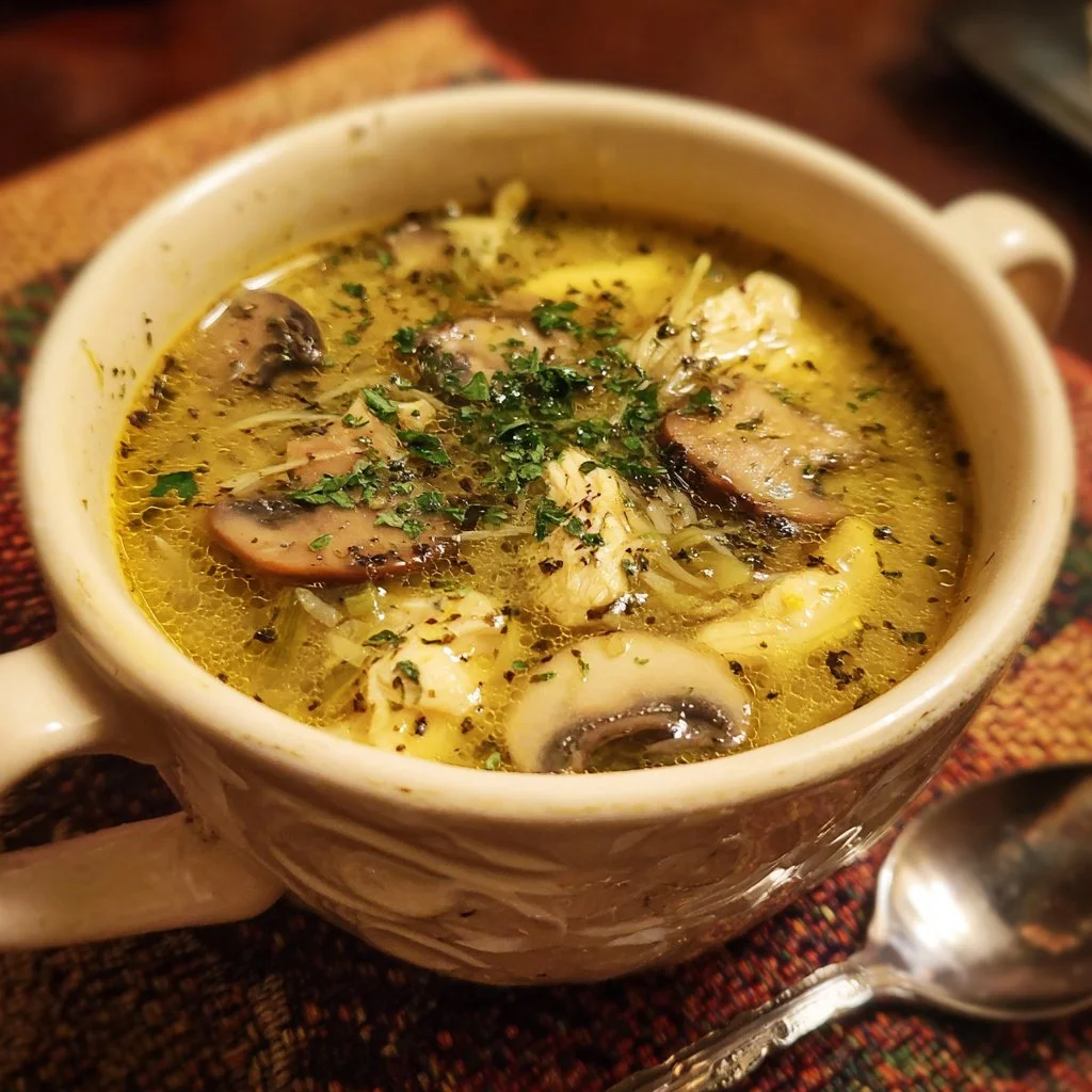 Bowl of clean chicken mushroom soup garnished with fresh herbs